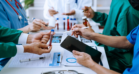 Medical team having a meeting with doctors in white lab coats and surgical scrubs seated at a table...