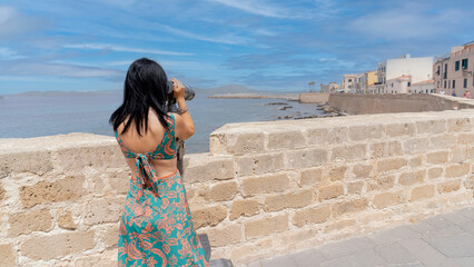 young girl observes the ramparts of Alghero with paid binoculars
