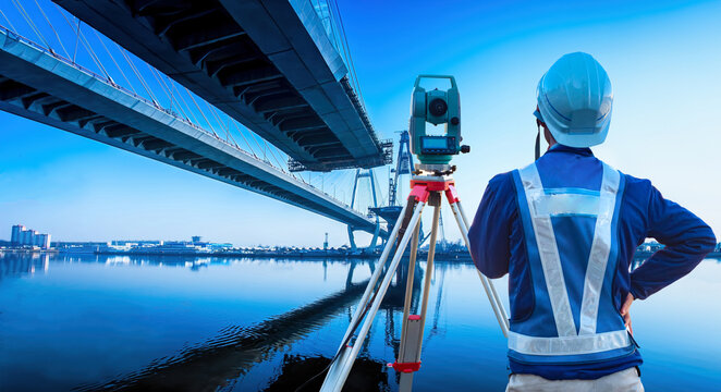 Bridge construction. Man with surveying equipment. Surveyor with his back to camera. Builder near bridge under construction. Surveyor for construction company. Road architecture. Surveyor near lake.