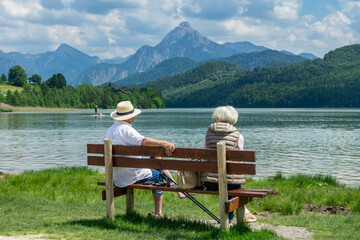 Urlaub im schönen Allgäu, Bayern: Zwei Senioren, Ehepaar sitzen auf Holzbank am Weißensee nähe...