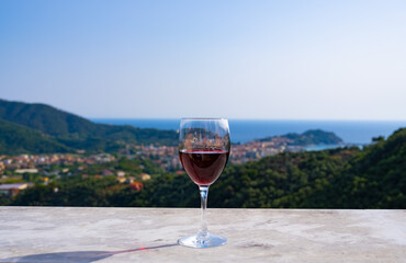 a glass of red wine against the backdrop of the sea and the town among the mountains