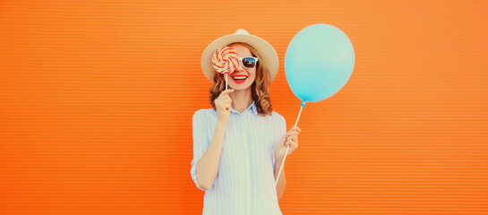Portrait of happy smiling young woman with blue balloon and lollipop wearing summer straw hat on...