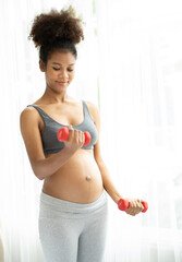 Obraz na płótnie Canvas Multiracial pregnant woman lifting dumbbell workout in fitness. Beautiful expectant mother in sportswear exercising weight training, portrait. Young multiethnic mom with healthy pregnancy lifestyle.