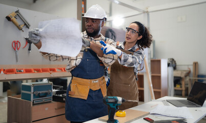 Female Latin carpenter and multiracial colleague working in carpenter's shop repair wood furniture. Hispanic woman design wooden craft in woodwork business. Diverse ethnic people in craftsman workshop