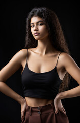 Classic studio portrait of a young brunette dressed in a black top, who is sitting on a chair against a black background. Generative AI.
