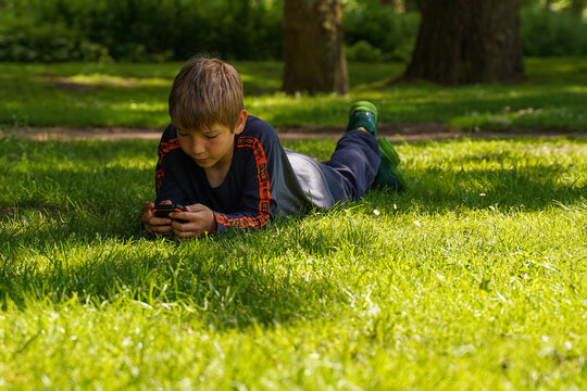 A teenager on the grass, bent over the phone, the problem of children's gambling addiction.