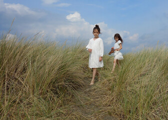 Two girls in white dresses walking between sand grass on dunes
