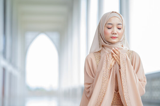 The image of an Asian Muslim woman in the Islamic religion in hijab in cream color. reading the Quran and having a happy Staying in a beautiful mosque, Arabic word translation: The Holy Al Quran.