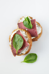 two mini sandwiches with beef and spinach on a white table