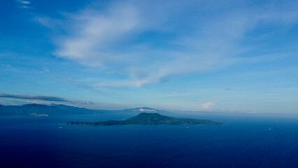 Tropical island in the middle of the sea. Aerial view of a green tropical island on the horizon surrounded by blue sea.