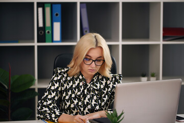 smiling blonde businesswoman with glasses using laptop in the office