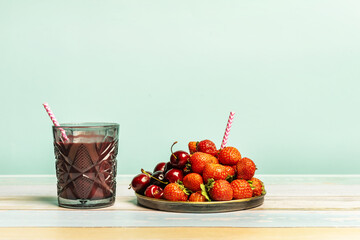 A glass of red berry detox juice with a straw, ripe red berries