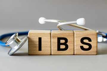 Medical stethoscope and wooden blocks with the inscription IBS, Abbreviation for irritable bowel syndrome, a chronic disease of the gastrointestinal tract of a functional nature, gray background