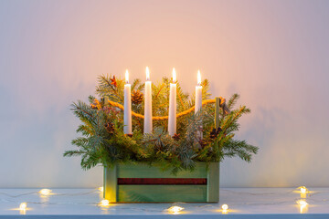 advent decoration with fir branches and four burning candles in wooden basket on white background