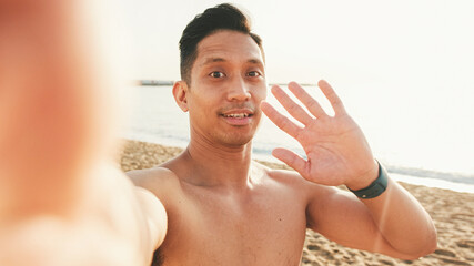Fototapeta na wymiar Close up of guy, an athlete with a naked torso standing on the beach makes a selfie on a smartphone
