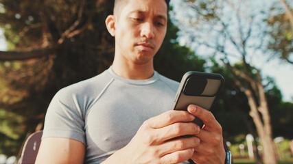 Guy in sportswear, an athlete sits on a bench in a city park, scrolls information, watches videos,...