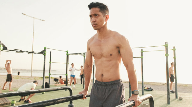 Guy, the athlete does push-ups on the parallel bars on the outdoor sports ground on a summer day