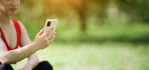 Young woman using smartphone after doing yoga outdoors in the park, sports yoga concept    