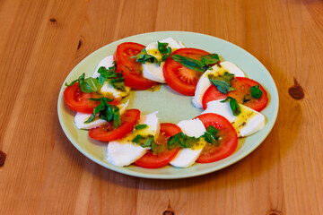 Italian caprese salad with tomatoes, mozzarella cheese and basil on a wooden table