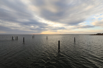 Obraz premium Scenic view of pilons in ocean beneath stormy sky at sunset