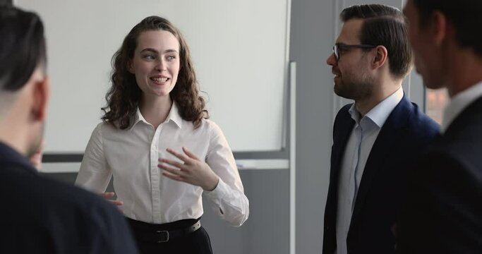 Positive pretty young professional woman talking to business partners on meeting, standing in office boardroom, telling about startup project, partnership terms to investors