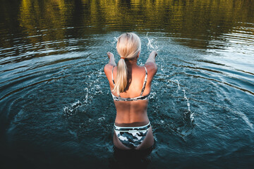 Fit blonde woman stands in the river water before entering for a swim