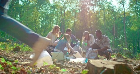 Teamwork of diverse volunteer puts dirty plastic bottles, rubbish in bag with garbage. Men and women helping with trash for eco friendly recycling. Concept of environmental pollution and ecology.