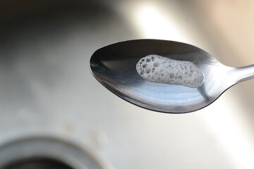 Spoon with soap foam in the steel sink background.