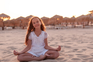 Fototapeta na wymiar beautiful caucasian girl at sunset on the beach doing yoga, dressed in all white