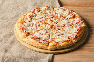 sliced pizza with tomatoes and ham on a wooden tray on the table