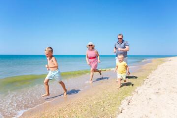 Elderly man and woman play with children along the seashore. A happy family laugh and joyfully run...