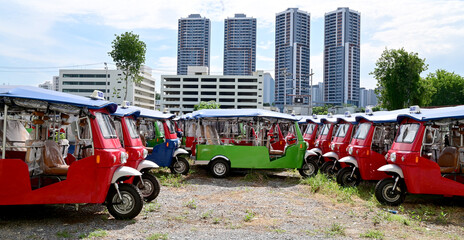 BANGKOK, THAILAND - JULY 10, 2023: Several Electric tuk tuks taxi stopped in the meadow with...