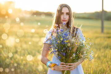 young woman in a wheat field with a bouquet of daisies