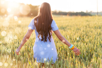 a young woman with long hair in a short dress walks through a wheat field
