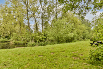 a bench in the middle of a grassy area with trees surrounding it and water running through the park's edge