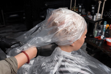 The hands of a professional hairdresser fix a plastic film on the client's head before dyeing her hair in a salon or barbershop