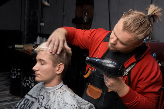 Stylish business barber Caucasian professional blow-drying hair to a client, a guy in a salon or a hairdresser before a haircut