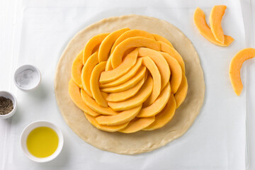 Obraz na płótnie Canvas Rolled out dough with pumpkin filling surrounded by spices and olive oil on a white wooden background, top view