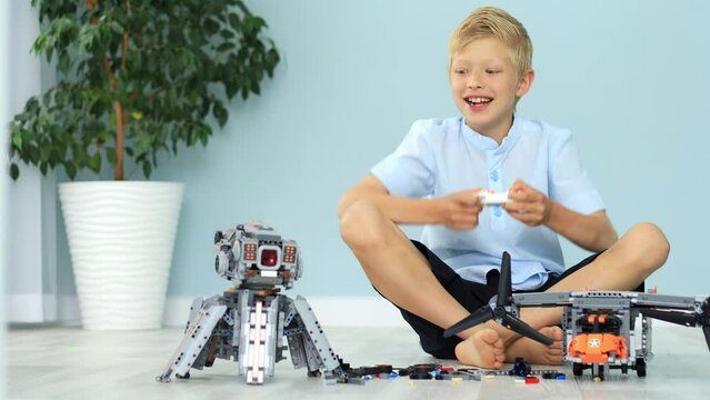 a joyful child boy is playing a robot from a radio-controlled constructor with a remote control, assembling it from the details of the house on the floor, a blonde child is playing at home