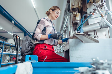 Woman worker in factory producing metal parts on punching machine