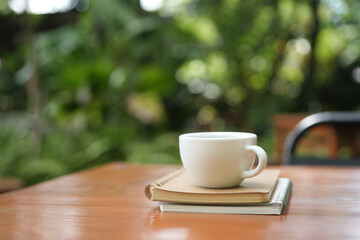 White coffee cup and bronze spoon on brown wooden table with green lush background