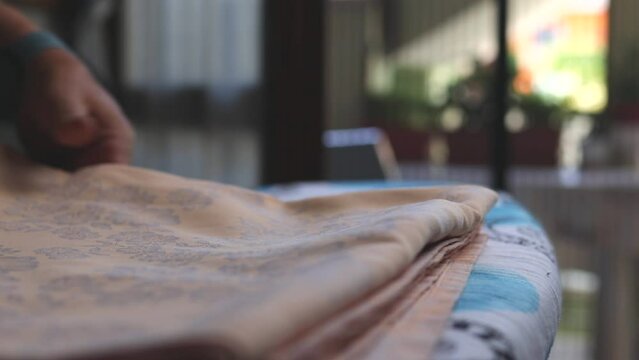 A woman folding a tablecloth on an ironing board after ironing it