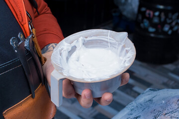 A barber man's hand holds a container of white dye for dyeing clients' hair at work