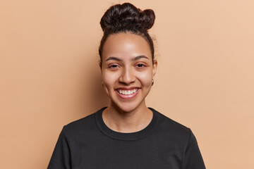 Portrait of cheerful Latin woman with hair bun smiles gladfully dressed in casual black t shirt...