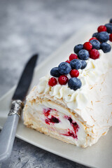 Meringue roll cake with cream, confiture and decorated with fresh blueberry and cranberry
