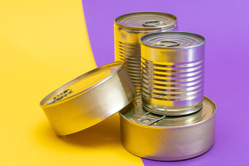 A Group of Stacked Tin Cans with Blank Edges on Split Yellow and Violet Background. Canned Food. Different Aluminum Cans for Safe and Long Term Storage of Food. Steel Sealed Food Storage Containers