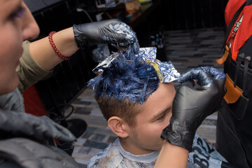 The process of dyeing hair in color for a young guy in a salon or barbershop at work service