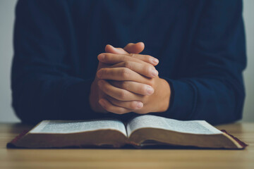 Man hands praying to god on the open bible on a wooden table. begging for forgiveness and believing...