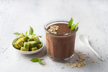 Chocolate smoothie or cocktail with frozen avocado and oatmeal garnished with mint leaves on a light blue table. vegan food - 621573574