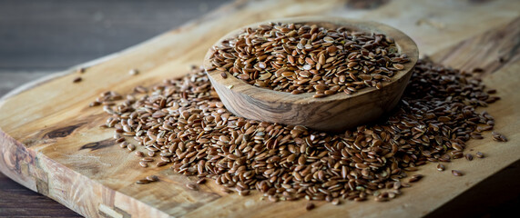 A narrow close up view of a small wooden bowl overflowing with whole flax seeds.